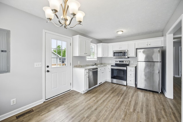 kitchen featuring appliances with stainless steel finishes, white cabinets, wood finished floors, and visible vents