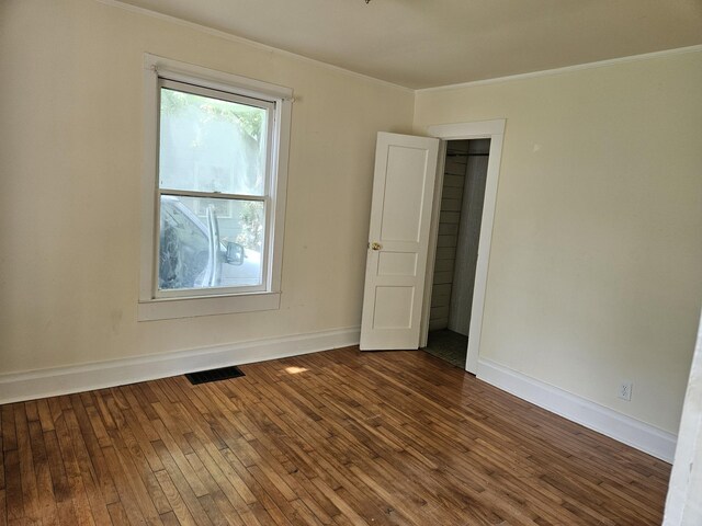 spare room featuring wood-type flooring, baseboards, visible vents, and ornamental molding
