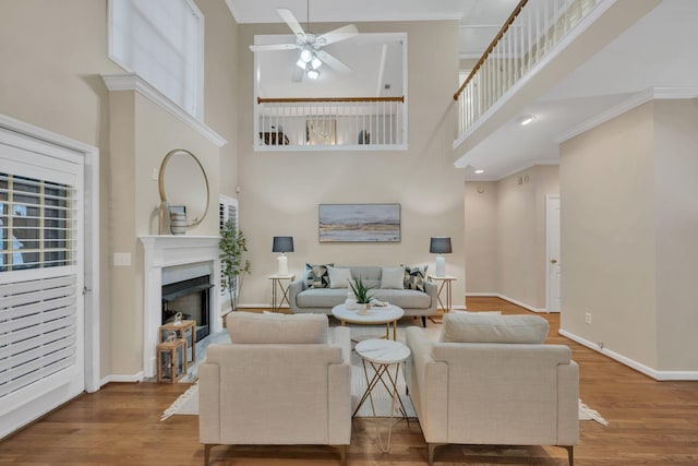 living room with ceiling fan, a towering ceiling, a fireplace, wood finished floors, and baseboards