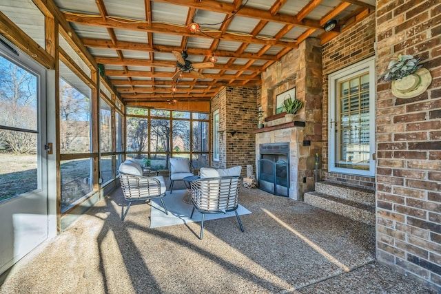 unfurnished sunroom featuring a ceiling fan, an outdoor living space with a fireplace, and a healthy amount of sunlight