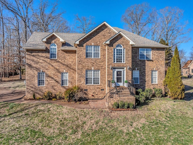 colonial home with brick siding, a front yard, and roof with shingles