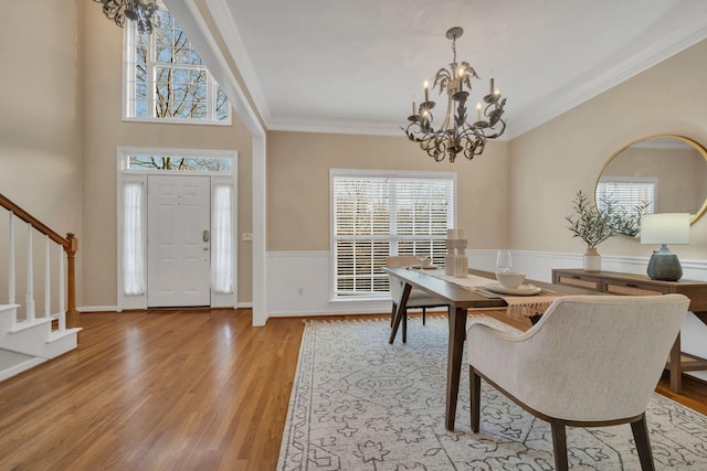 foyer with wood finished floors, stairway, a wainscoted wall, a chandelier, and ornamental molding