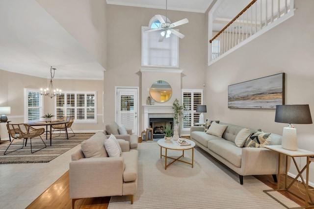 living room with crown molding, a fireplace, wood finished floors, baseboards, and ceiling fan with notable chandelier
