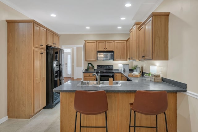 kitchen with a kitchen bar, dark countertops, a sink, black appliances, and a peninsula