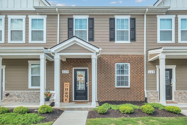 doorway to property featuring board and batten siding, brick siding, and a porch