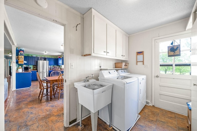 laundry room with ornamental molding, stone finish floor, a textured ceiling, washing machine and clothes dryer, and cabinet space