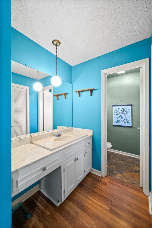 bathroom featuring vanity, wood finished floors, toilet, baseboards, and a textured ceiling