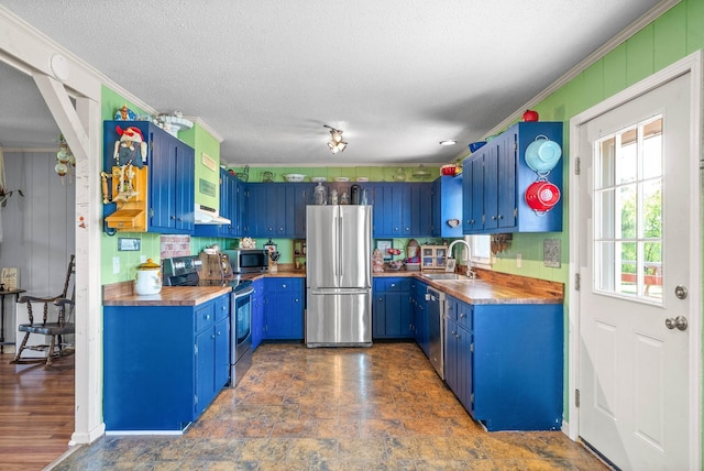 kitchen with appliances with stainless steel finishes, a sink, a textured ceiling, blue cabinetry, and butcher block counters