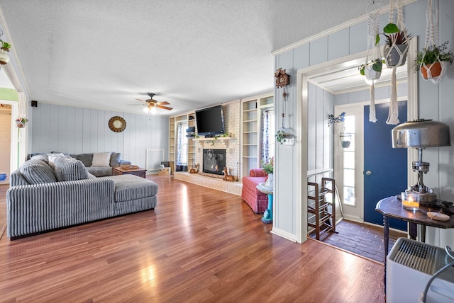 living room with a fireplace, a textured ceiling, a ceiling fan, wood finished floors, and ornamental molding