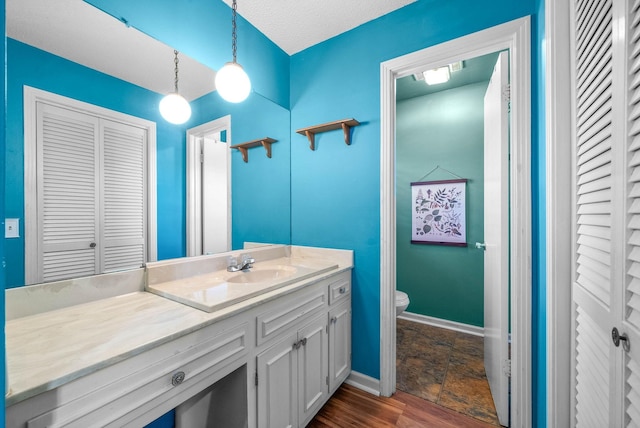 bathroom with a closet, vanity, toilet, baseboards, and stone finish flooring