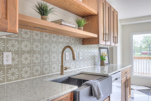 411 Willow Lake Dr, Portland, TN 37148 - kitchen with stainless steel dishwasher, brown cabinetry, light stone counters, a sink, and backsplash