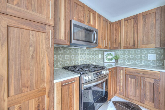 411 Willow Lake Dr, Portland, TN 37148 - kitchen featuring light stone counters, backsplash, stainless steel appliances, and brown cabinetry