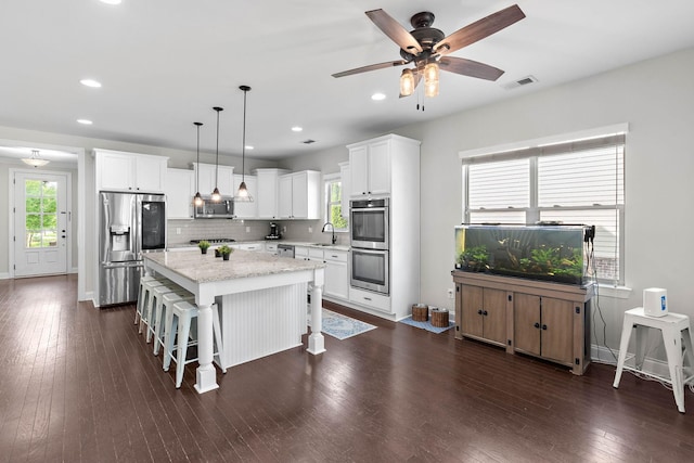 kitchen featuring backsplash, visible vents, appliances with stainless steel finishes, a center island, and dark wood-type flooring