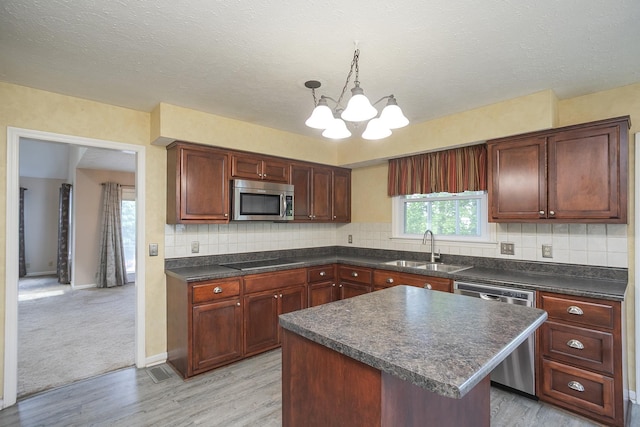 kitchen with appliances with stainless steel finishes, a sink, a chandelier, light wood-style flooring, and dark countertops