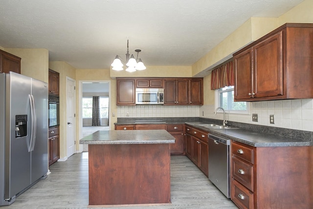 kitchen with stainless steel appliances, a sink, dark countertops, light wood-style floors, and a chandelier