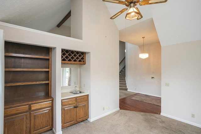 indoor wet bar with light carpet, stairs, ceiling fan, baseboards, and high vaulted ceiling