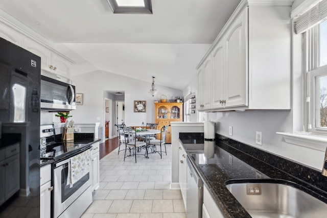 kitchen with white cabinets, appliances with stainless steel finishes, lofted ceiling, and dark stone countertops