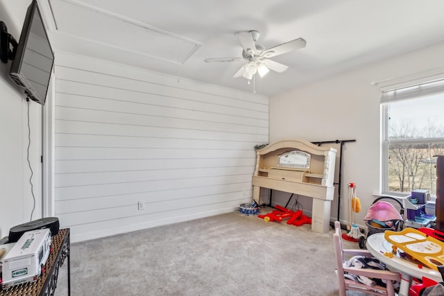 carpeted bedroom featuring ceiling fan, wood walls, and attic access