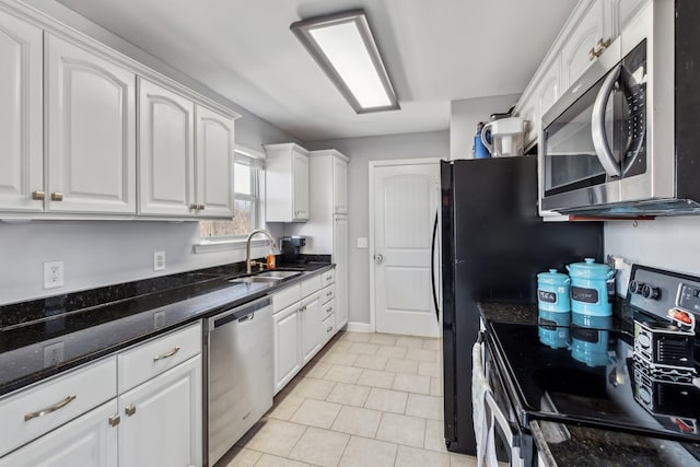 kitchen with white cabinets, appliances with stainless steel finishes, a sink, dark stone countertops, and light tile patterned floors