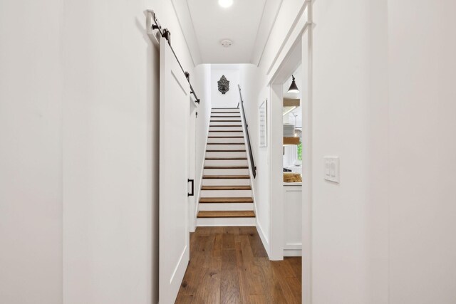 hall with baseboards, a barn door, wood finished floors, and stairway