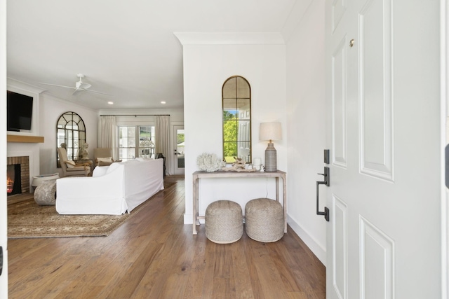 foyer entrance featuring a fireplace, a ceiling fan, recessed lighting, wood finished floors, and ornamental molding