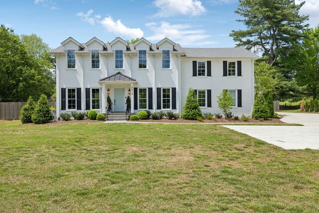 colonial house with fence, brick siding, and a front yard