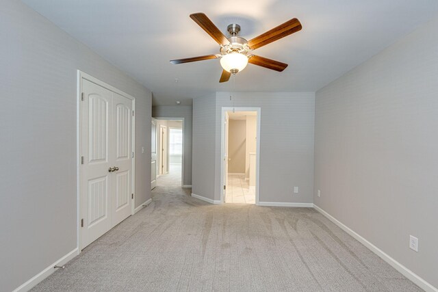 unfurnished bedroom featuring a ceiling fan, baseboards, light colored carpet, and ensuite bathroom