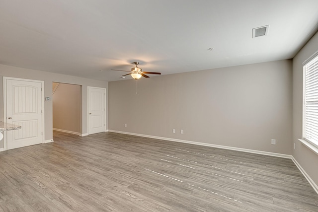 spare room with ceiling fan, plenty of natural light, light wood-style flooring, baseboards, and visible vents