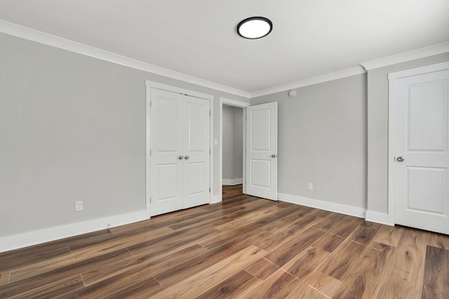 unfurnished bedroom featuring crown molding, baseboards, wood finished floors, and a closet