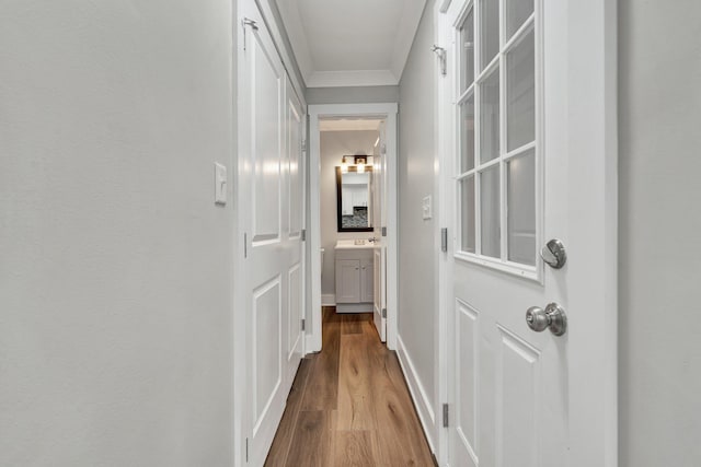 hallway with crown molding, a sink, baseboards, and wood finished floors