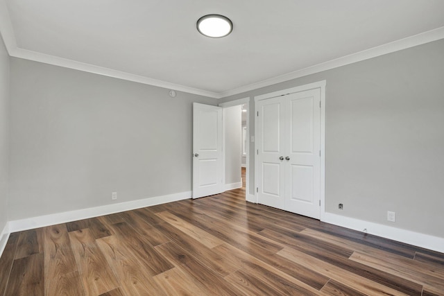 unfurnished bedroom with crown molding, baseboards, a closet, and dark wood-style flooring