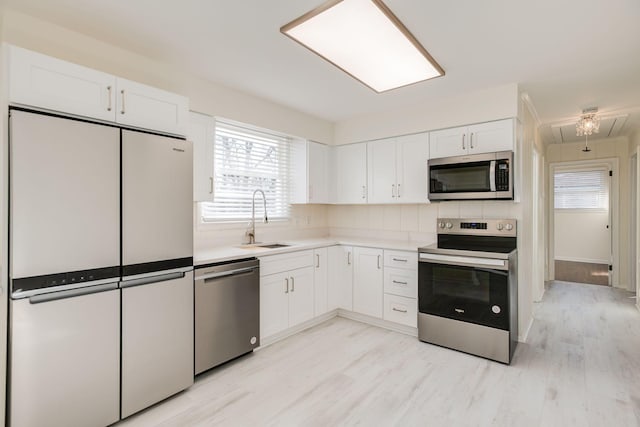 kitchen with light countertops, white cabinets, a sink, light wood finished floors, and stainless steel appliances