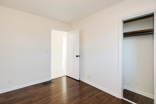 unfurnished bedroom featuring visible vents, baseboards, dark wood-style floors, and a closet