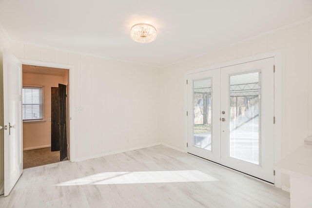 unfurnished room with a notable chandelier, ornamental molding, french doors, and light wood-type flooring