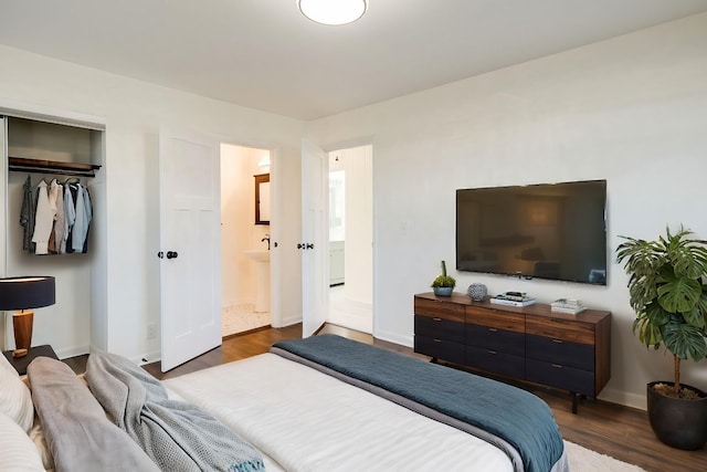 bedroom featuring dark wood-type flooring, baseboards, ensuite bathroom, and a closet