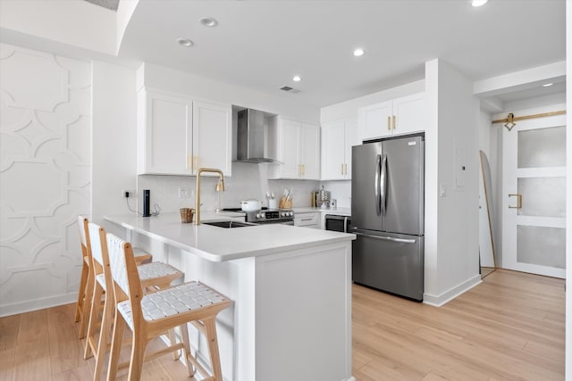 1510 Demonbreun St Unit 807, Nashville, TN 37203 - kitchen featuring a peninsula, wall chimney range hood, light wood-type flooring, recessed lighting, and stainless steel appliances