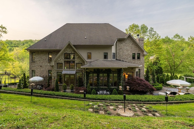 rear view of house featuring a lawn, a chimney, a sunroom, and a shingled roof