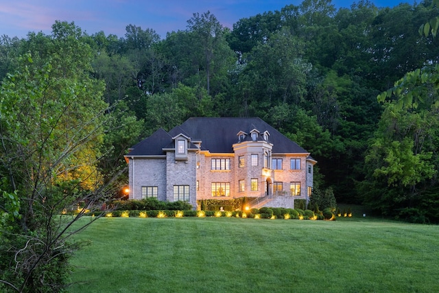 rear view of property with a lawn, brick siding, and a wooded view
