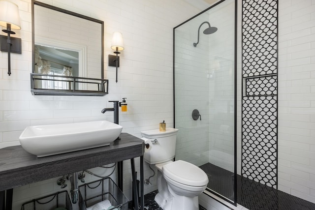 bathroom with a sink, a stall shower, toilet, and tile walls