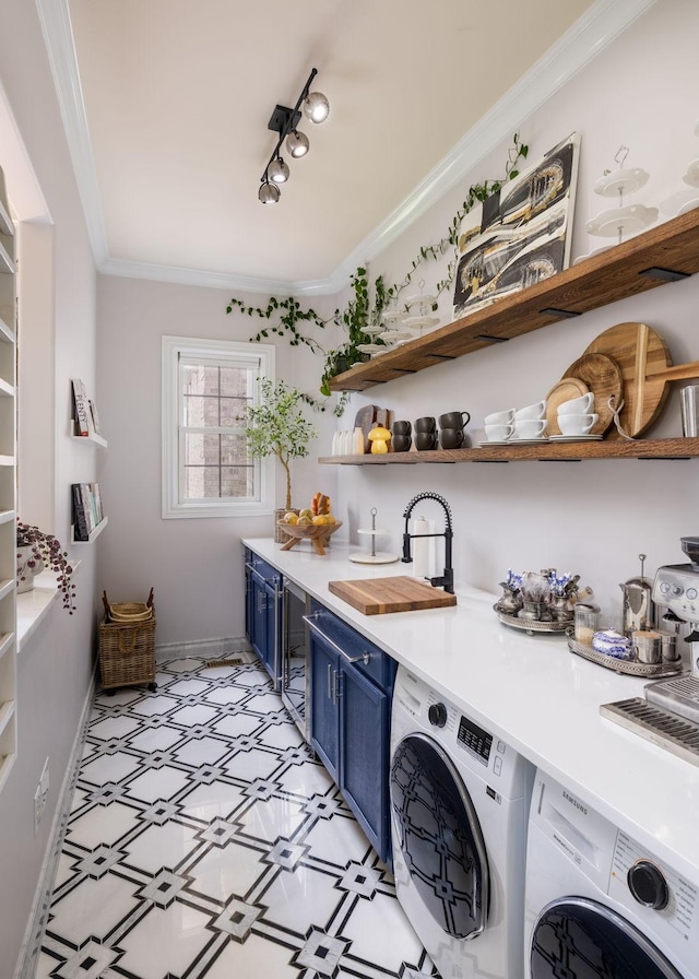 clothes washing area with laundry area, ornamental molding, light floors, washing machine and clothes dryer, and a sink