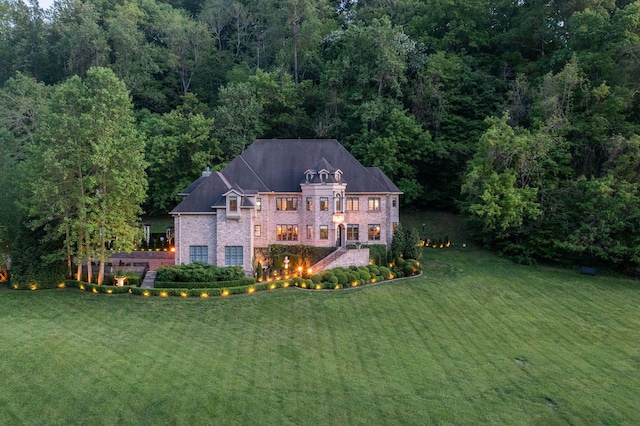 back of property featuring a yard, brick siding, and a wooded view