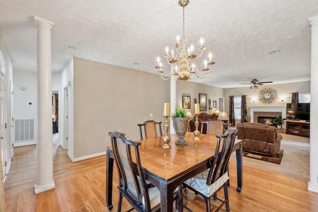dining area featuring visible vents, decorative columns, a fireplace, a textured ceiling, and ceiling fan with notable chandelier