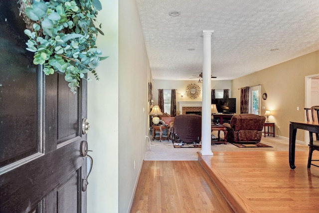 foyer with light wood-type flooring, a textured ceiling, baseboards, and a brick fireplace