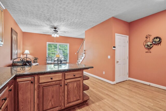 kitchen featuring baseboards, ceiling fan, a textured ceiling, brown cabinets, and light wood-style flooring