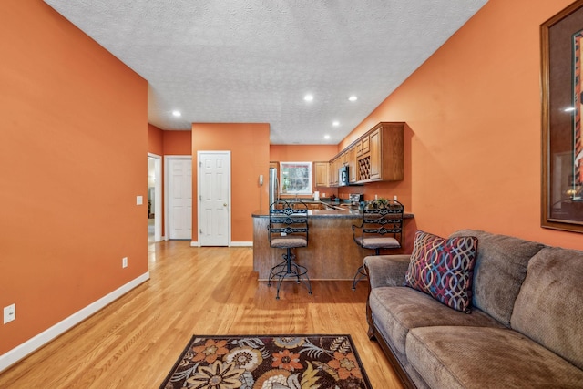 living area with light wood-type flooring, recessed lighting, a textured ceiling, and baseboards
