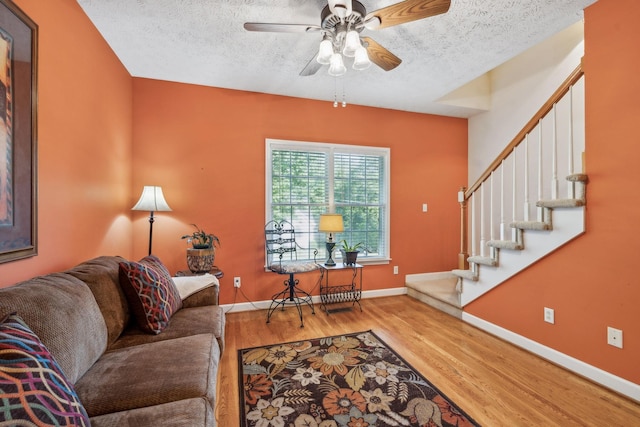 living area with ceiling fan, a textured ceiling, baseboards, wood finished floors, and stairway