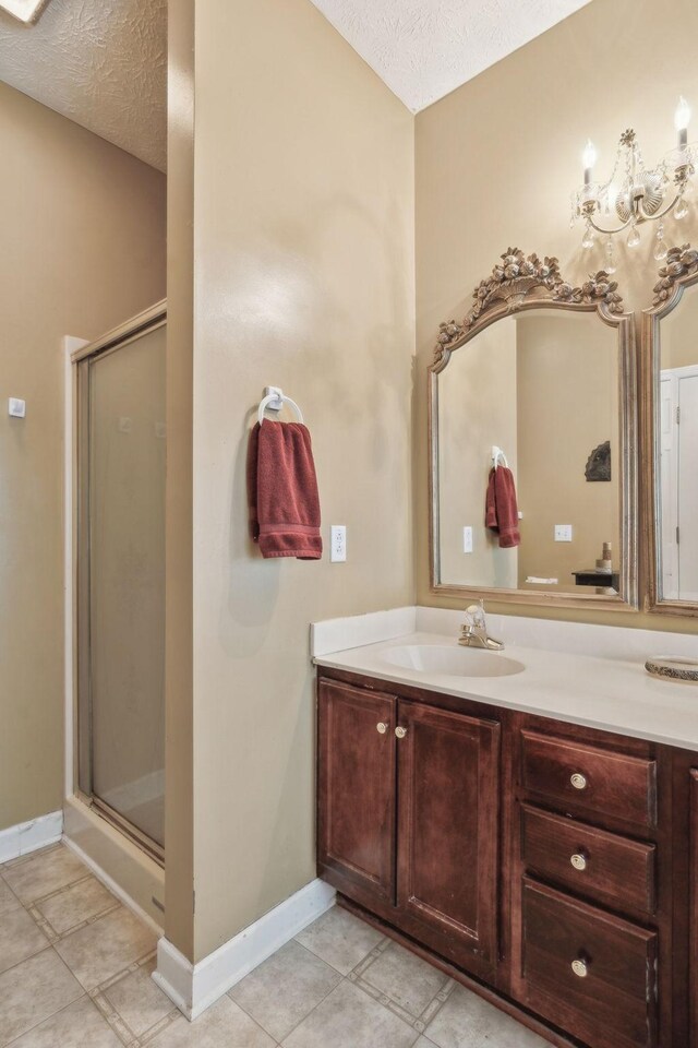 full bath with vanity, baseboards, a textured ceiling, and a stall shower