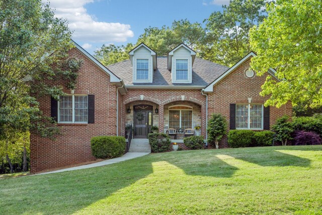 view of front of property featuring roof with shingles, a porch, brick siding, and a front yard