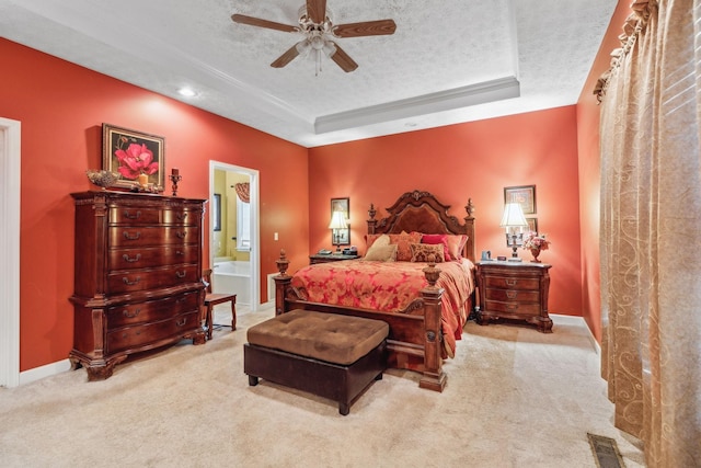 carpeted bedroom with a textured ceiling, a tray ceiling, baseboards, and ensuite bath