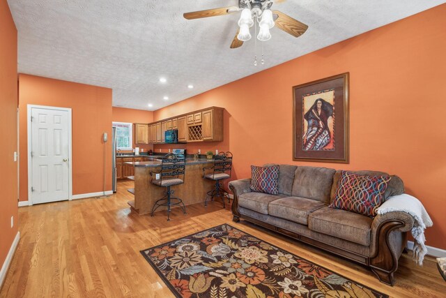 living area with baseboards, a ceiling fan, light wood-type flooring, and a textured ceiling